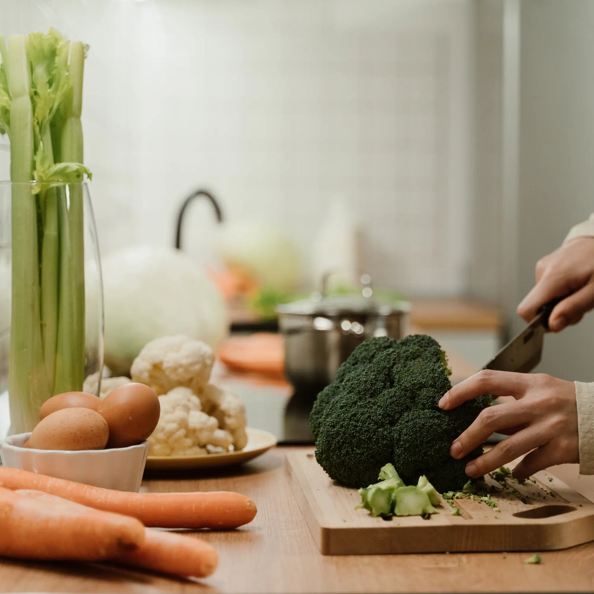 Hands cutting fresh broccoli among vegetables in a kitchen